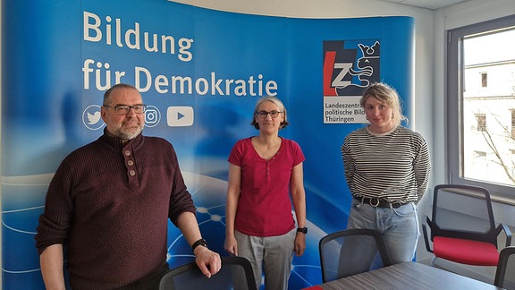 Die MitarbeiterInnen der Landeszentrale für politische Bildung in Thüringen Wieland Koch, Anja Zachow und Franziska Gräfenhan stehen vor dem Schriftzug "Bildung für Demokratie"