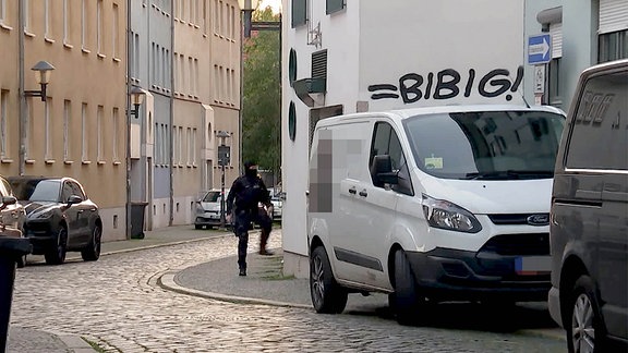 Ein Polizist steht in einer Gasse vor einem Wohnhaus. 