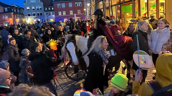 Menschenmenge mit Laternen auf dem Herderplatz in Weimar - Ein Mädchen mit einem roten Umhang auf einem Pferd reitet in der Menge