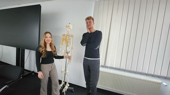 Eine Frau und ein Mann neben dem Modell eines Skeletts.