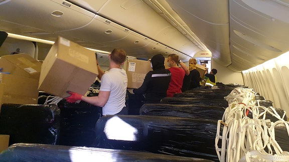 Männer stehen in der Kabine eines Passagierflugzeugs und entladen Kartons