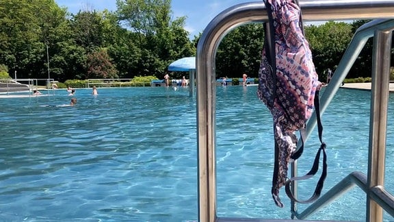 Ein Bikini-Oberteil hängt auf einem Geländer in einem Schwimmbad.