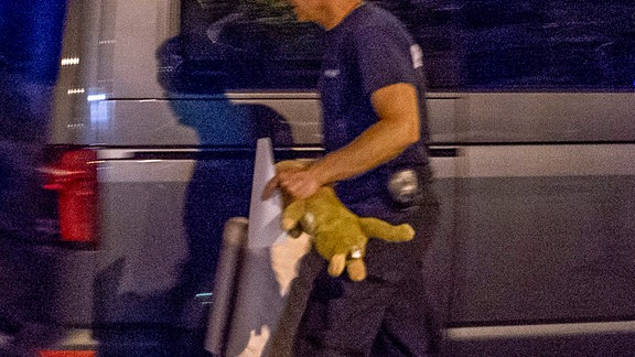 Ein Polizist hält einen Teddybär in der Hand.