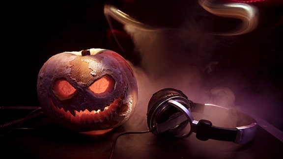 Symbolbild Halloween-Party -Leuchtender Kürbis, daneben liegen Kopfhörer