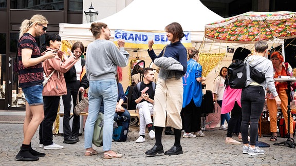 Junge Menschen gebärden vor einem Zelt mit der Aufschrift "Grand Beauty"