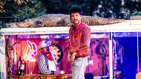 Zwei Schauspieler als Cowboysw verkleidet, im Hintergrund liegt ein Alligator