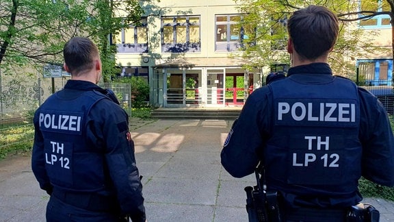 Zwei Polizisten stehen vor einer Schule.
