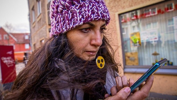 Eine Frau mit Blinden-Anstecker an ihrem Schal schaut auf ihr Handy.