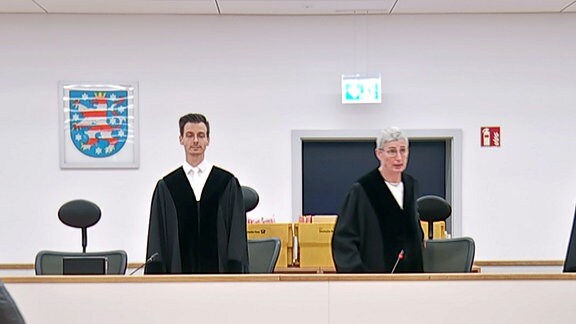 Mehrere Menschen stehen in einem Gerichtssaal in Erfurt.