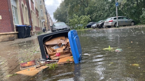 Eine umgekippte Mülltonne, eine überflutete Straße.