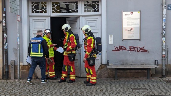 Feuerwehrleute stehen vor einer Eingangstür zu einem Haus.
