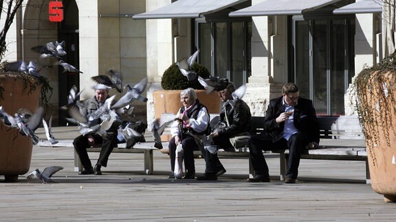 Passanten sitzen auf dem Vorplatz des Erfurter Haubahnhofs essen und füttern Tauben