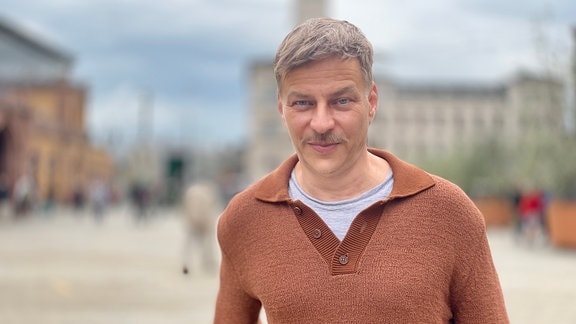 Tom Wlaschiha vor dem Hauptbahnhof in Erfurt. Er trägt einen braunen Pullover.