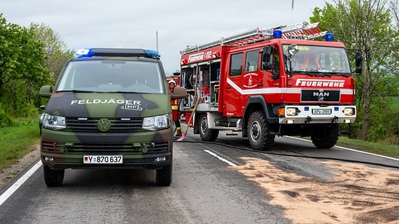 Ein Feldjäger-Auto steht neben einem Feuerwehrauto auf einer Straße.