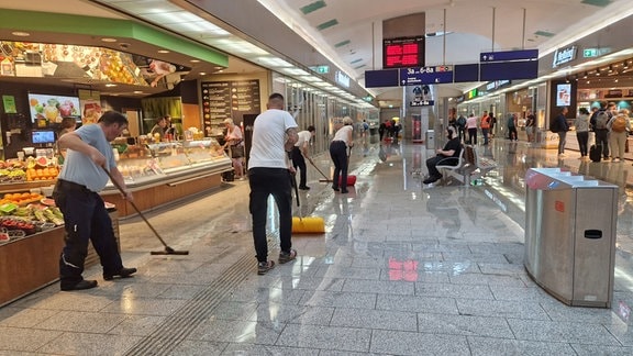 Mitarbeitende von Bahn und Geschäften kehren Wasser aus der Ladenzeile nach einer Überschwemmung im Bahnhofsgebäude im Hauptbahnhof Erfurt.