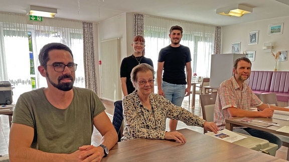 Menschen sitzen in einem Wahllokal und schauen in die Kamera