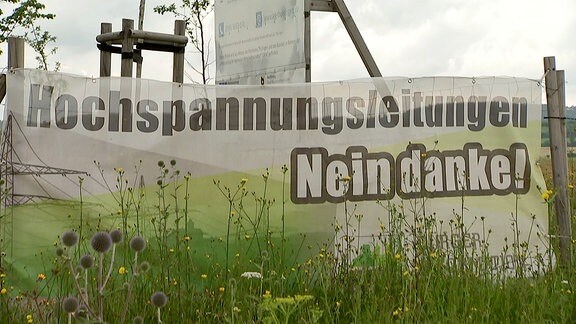 Ein Banner vor einem Bauschild: Protest gegen eine Hochspannungsleitung in Thüringen