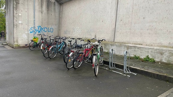 Fahrräder stehen vor einer Betonmauer in einem Ständer.