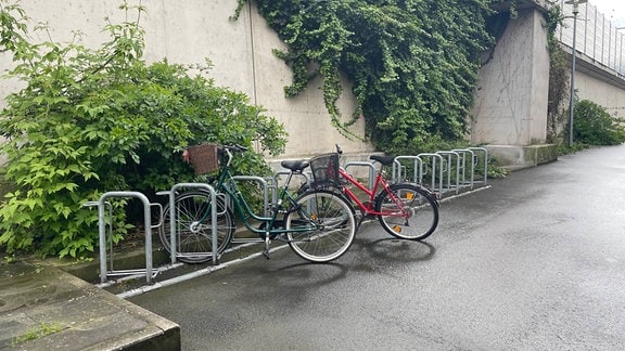 Ein Fahrrad steht vor einer Betonmauer in einem Ständer.