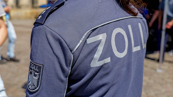 Eine Frau trägt Einsatzbekleidung vom Zoll mit Logo und Rückenaufschrift.
