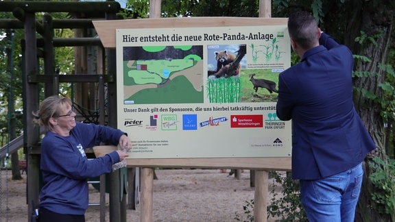 Zwei Menschen stehen vor einem Schild.