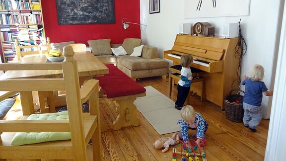 Drei Kinder spielen in einem großen Wohnzimmer mit Tisch, Sofa und Klavier.