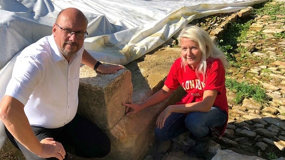 Ein Mann und eine Frau knien an einem alten Stein-Fundament