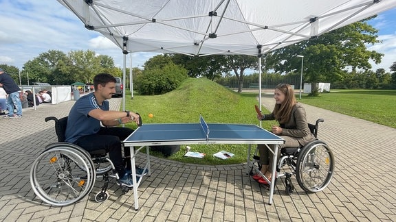 Ein Mann und eine Frau im Rollstuhl spielen Tischtennis.