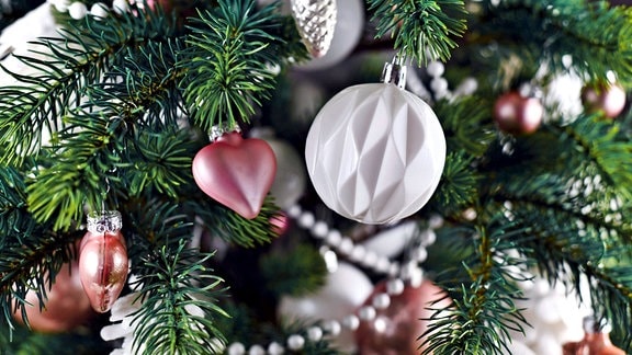 Nahaufnahme des geschmückten Weihnachtsbaums mit rosa und weißem Baumschmuck wie Kugeln, Sternen und Perlengirlande.