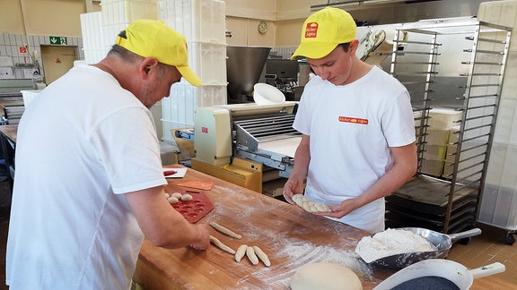 In einer Bäckerei fertigen zwei Männer verschiedene Backwaren.