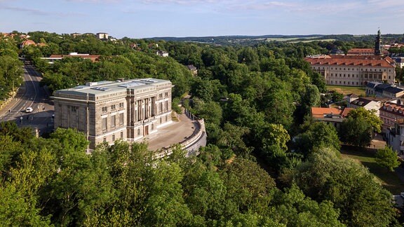 Luftaufnahme eines von Bäumen umgebenen schlossähnlichen Gebäudes mit großer Terrasse 