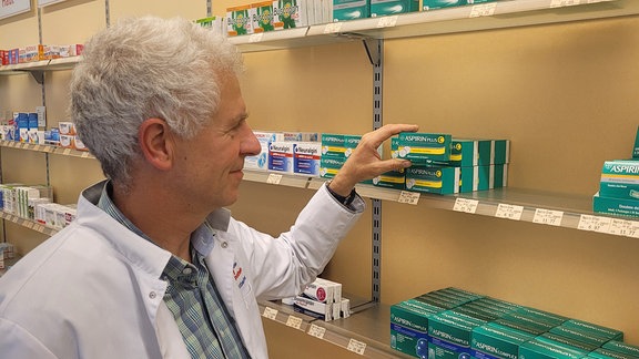 Apotheker Markus Wurzbacher nimmt eine Packung Aspirin aus einem Regal