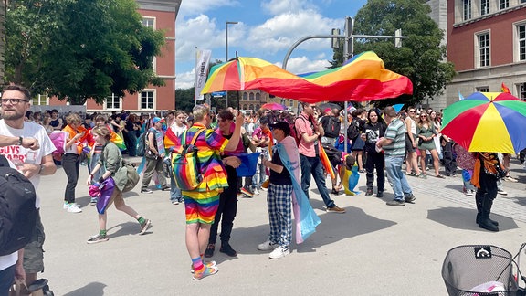 CSD Weimar 2024: Menschen stehen buntgekleidet unter einem Regenschirm.