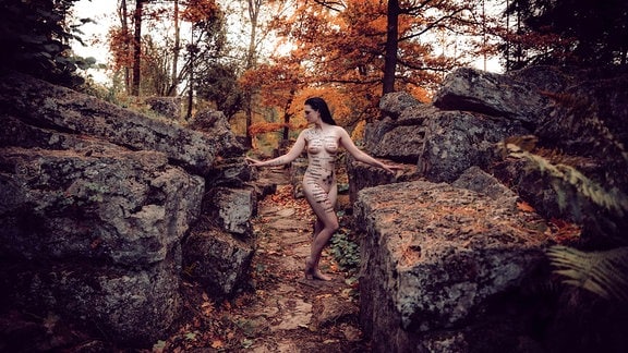 Eine junge Frau mit schwarzen Haaren nackt im Wald