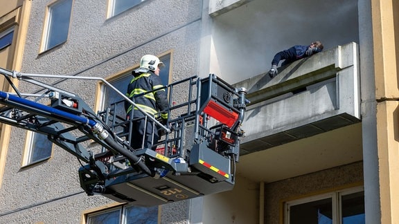 Ein Feuerwehrmann steht auf einer Leiter an einem Balkon. 