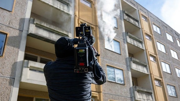 Ein Kameramann filmt ein Wohnhaus, aus dem Rauch dringt. 