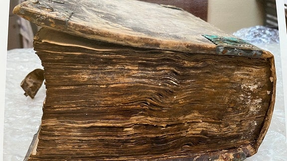 Ein mit Schlamm bedecktes altes Buch leigt auf einem Tisch.