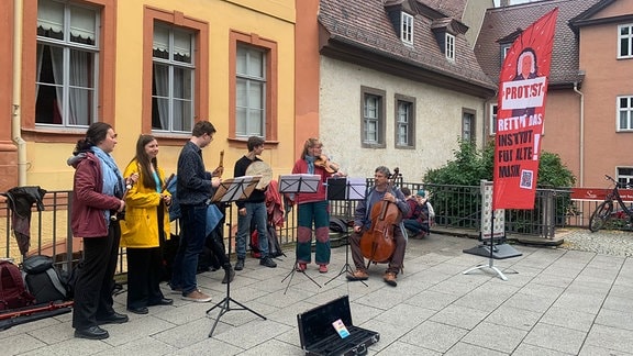 Junge Musikerinnen und Musiker spielen auf einem Platz in Weimar, im Hintergrund ein Banner "Protest"