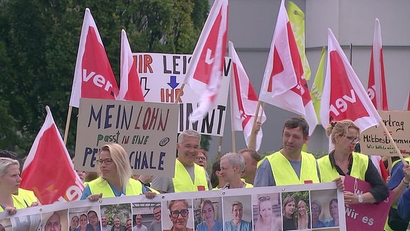 Mitarbeitende des Hufeland-Klinikums in Weimar stehen mit Fahnen und Transparenten vor dem Gebäude