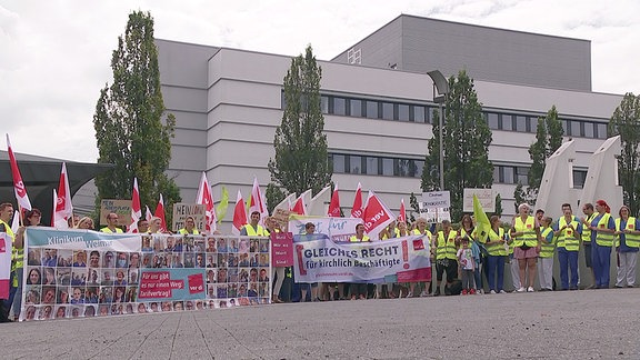 Mitarbeitende des Hufeland-Klinikums in Weimar stehen mit Fahnen und Transparenten vor dem Gebäude