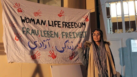 Eine junge Frau mit Brille auf einer Kundgebung neben einem Banner mit der Aufschrift - Frau Leben Freiheit.