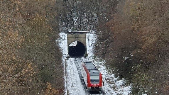 Ein Zug fährt durch verschneite Landschaft in einen Tunnel ein.