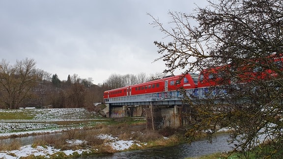 Ein Zug fährt überquert auf einer Brücke einen Fluss im Winter.