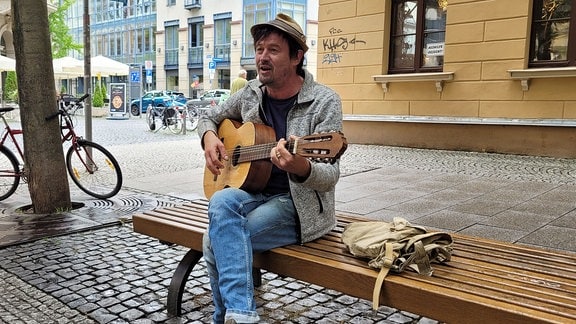 Moritz Rabe spielt Gitarre auf einer Bank in der Weimarer Schillerstraße.