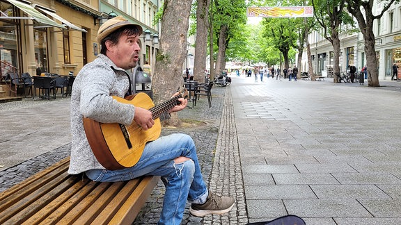 Moritz Rabe spielt Gitarre auf einer Bank in der Weimarer Schillerstraße.