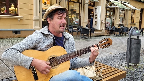 Moritz Rabe spielt Gitarre auf einer Bank in der Weimarer Schillerstraße.