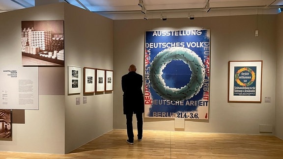 Ein Mann steht in einem Ausstellungsraum in dem Plakate hängen