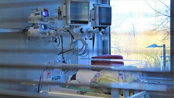 ein Baby in einem Inkubator-Bett hinter einer Scheibe