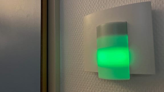 Grün leuchtende Lampe an der Wand vor einem Patientenzimmer.