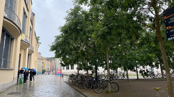 Studierende stehen vor dem Eingang der Universität im Regen.